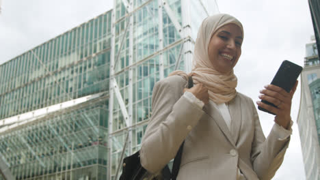 Muslim-Businesswoman-Celebrating-Good-News-On-Mobile-Phone-Standing-Outside-Office-In-City